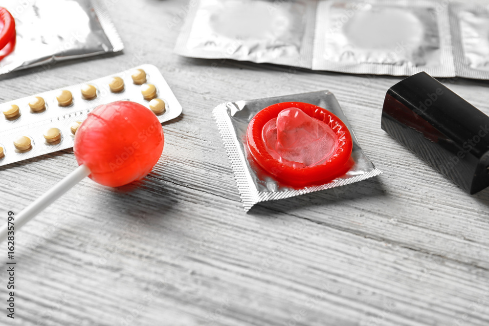 Condoms, lollipop and birth pills on wooden table. Contraception concept