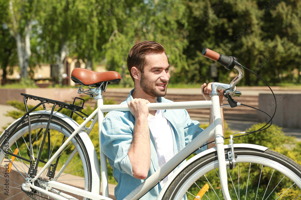 Handsome young man carrying bicycle outdoors