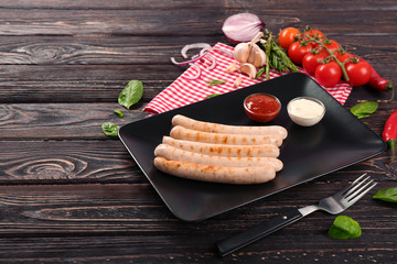 Sticker - Black square plate with delicious grilled sausages on wooden table