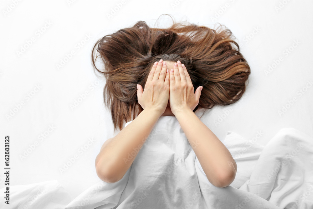 Young woman lying in bed and covering face with hands