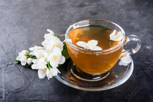 Cuadros en Lienzo Cup of tea and jasmine flowers on a dark concrete background