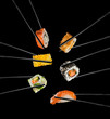 Sushi pieces placed between chopsticks, on black background