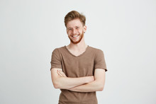 Portrait Of Happy Cheerful Young Man With Beard Smiling Looking At Camera With Crossed Arms Over White Background.