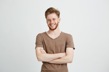 portrait of happy cheerful young man with beard smiling looking at camera with crossed arms over whi