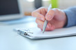 © cameravit - Male hand holding silver pen ready to make note in a clipboard. Businessman or employee at workplace writing business ideas, plans or tasks. Office life or education concept.