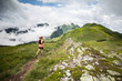 young woman running alone on extreme adventure ultra trail with high mountain scenery and blue sky