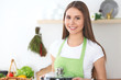 © rogerphoto - Young happy woman in a green apron cooking in the kitchen. Housewife found a new recipe for her soup. Healthy food and vegetarian concept