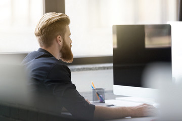 Wall Mural - Young bearded man sitting at his desk