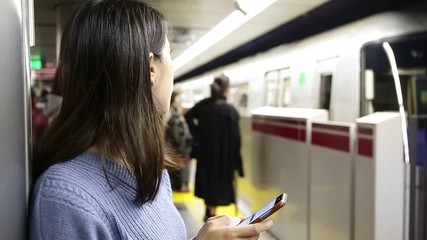 Wall Mural - Woman using the cellphone when waiting for ride at subway station