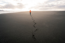 Guy In Iceland Walking On Empty Black Sand Beach Into Sunset Leaving Footprints