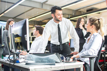 Wall Mural - Businessman leaning over female colleague's desk  flirting in office while working on project together.