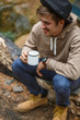 © horimono - Happy hiking man sits by firecamp near tent and drinks from mug