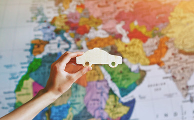 Hand with wooden car sign on world map. Renting and travelling by car