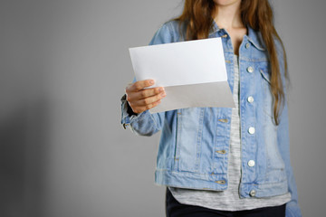 Wall Mural - The girl in the blue denim shirt holds the white empty piece of paper. Ready for your design. Closeup. Isolated