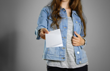 Wall Mural - The girl in the blue denim shirt holds the white empty piece of paper. Ready for your design. Closeup. Isolated