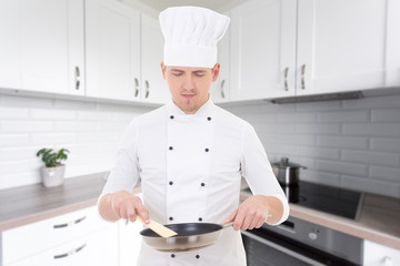 Wall Mural - man chef in uniform holding frying pan in modern kitchen