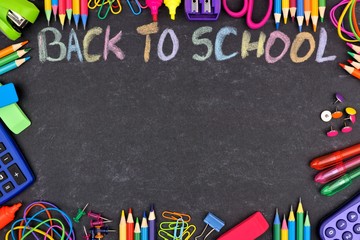 School supplies frame with Back To School written in colorful chalk with against a chalkboard background