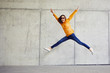 canvas print picture - Ecstatic young woman jumping in joy and raising arms in urban outside setting