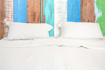 A white bed with 2 pillows on wooden wall room background