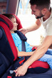 © ArtFamily - Smiling son in infant car seat being put in back of car by caring father