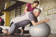 © liderina - Senior man workout in rehabilitation center. Personal trainer helping senior man on Pilates ball.