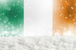 Defocused Ireland flag as a winter Christmas background with falling snow, snowdrift and bokeh