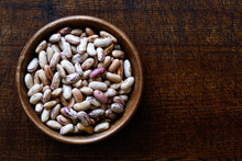Dry Pinto Beans In Dark Wooden Bowl Isolated On Dark Brown Wood From Above.