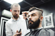 © nagaets - Master cuts hair and beard of men in the barbershop, hairdresser makes hairstyle for a young man