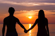Romantic Valentine's Day scene of a young couple silhouettes holding hands by the sea staring at colorful sunset in the island of Koh Phangan, Thailand. Love scene concept