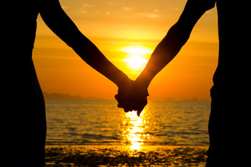 Perfect scene for Valentines Day with the silhouette of a couple holding hands at sunset by the sea in the island of Koh Phangan, Thailand. Romance, love concept