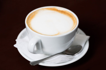 Poster - White cup with coffee and spoon saucer on a dark brown table