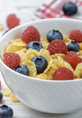 Wall Mural - Cornflakes with fresh berries raspberry and blueberry in white bowl on the table. Healthy Breakfast. Selective focus. Top view