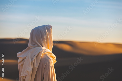 Fotografía Jesus Christ looks out at a setting sun in the sand dunes.