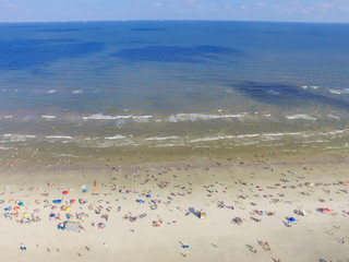 Aerial view beach shoreline on sunny summer day with people bathing, sunbathing, playing volley and relax in Galveston, Texas. Colorful umbrellas, lounge chairs. Holiday maker, summer vacation concept