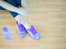 Woman Leg Wearing Purple Shoes With Bottle Of Water On Wooden Floor Background. Exercise Concept.