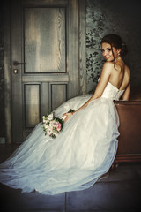 Wall Mural - Beautiful bride sits in a leather chair in a dark room