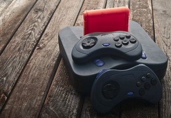 Vintage game console with gamepads and cartridge on a wooden table.
