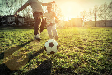 Father and son playing together with ball in football under sun