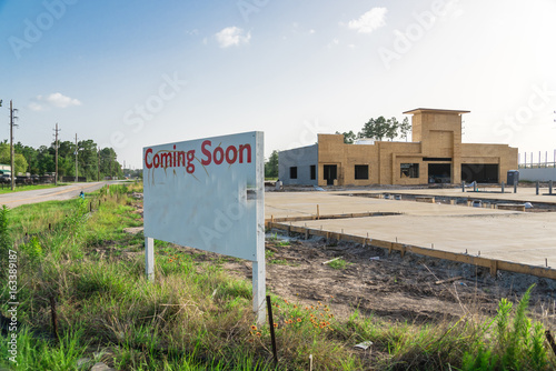 Fotografie, Obraz Coming Soon sign stands at the street corner/intersection, under construction convenience store is in background