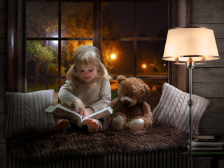 little girl reads a book, drives a finger over the lines. The child is sitting with a Teddy bear. Cozy children room, beautiful window, evening