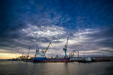 Cargo cranes transship bulk in the dock of Industrial Port on sunset with epic skyline