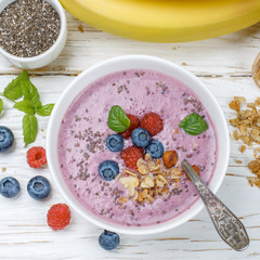 Wall Mural - Healthy delicious smoothie from banana and fresh berries raspberry and blueberry granola with Chia seeds and mint leaves in white bowl