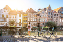 Sunrise View On The Water Channel With Beautiful Old Buildings With Woman Standing Near The Bicycles In Gent City