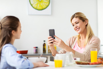 Wall Mural - woman photographing daughter by smartphone at home