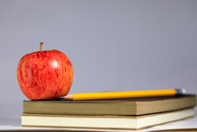 A Red Apple On A Stack Of Books And Pencil With Gray Background