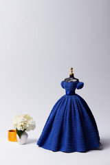 Wall Mural - Fashion Concept. Crochet blue ball gown on a mannequin and vase with flowers. Clothes for 11-inch doll. Cover for a magazine