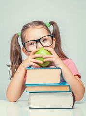 Wall Mural - playful beautiful cute little girl behind books holding green apple