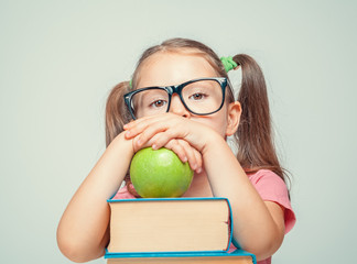 Wall Mural - thoughtful beautiful cute little girl with green apple and thick books looking at camera
