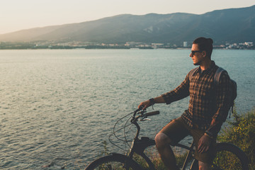 Wall Mural - Adult Male Standing With Bike On Coast And Enjoying View of Nature Sunset Vacation Traveling Relaxation Resting Concept