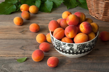 Fresh apricots with leaves in a bowl on a wooden background